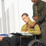 man in rolstoel aan het werk aan het werk en bijgestaan door een collega